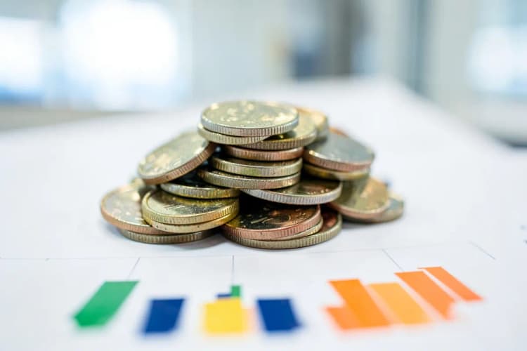Uma pilha de moedas de diferentes tamanhos e cores empilhadas em cima de um gráfico de barras simples.